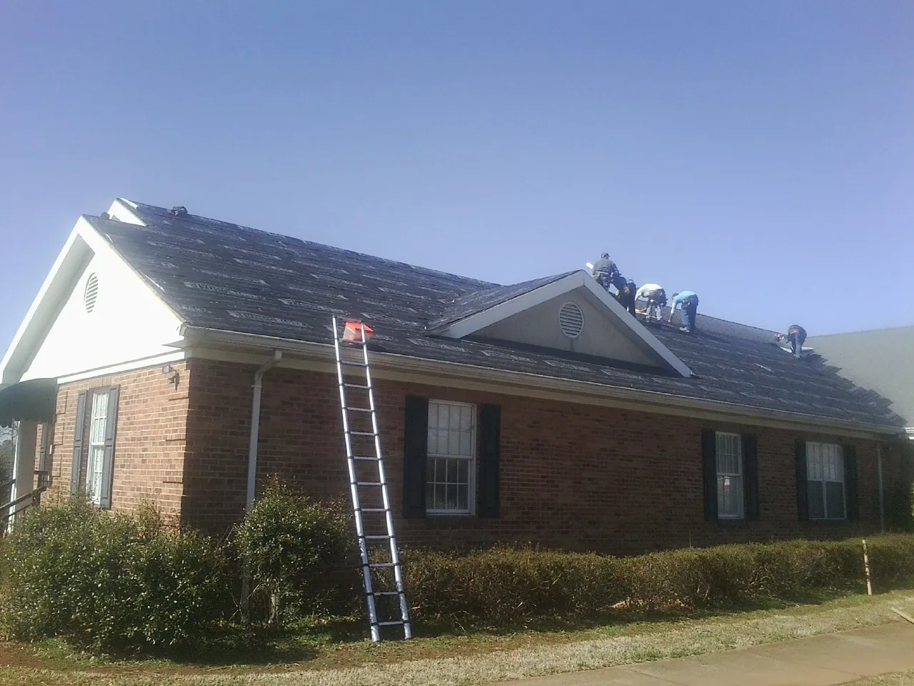Crew tearing shingles off a brick ranch roof with a ladder set — Metal Roof Repair work by our crew in Poland