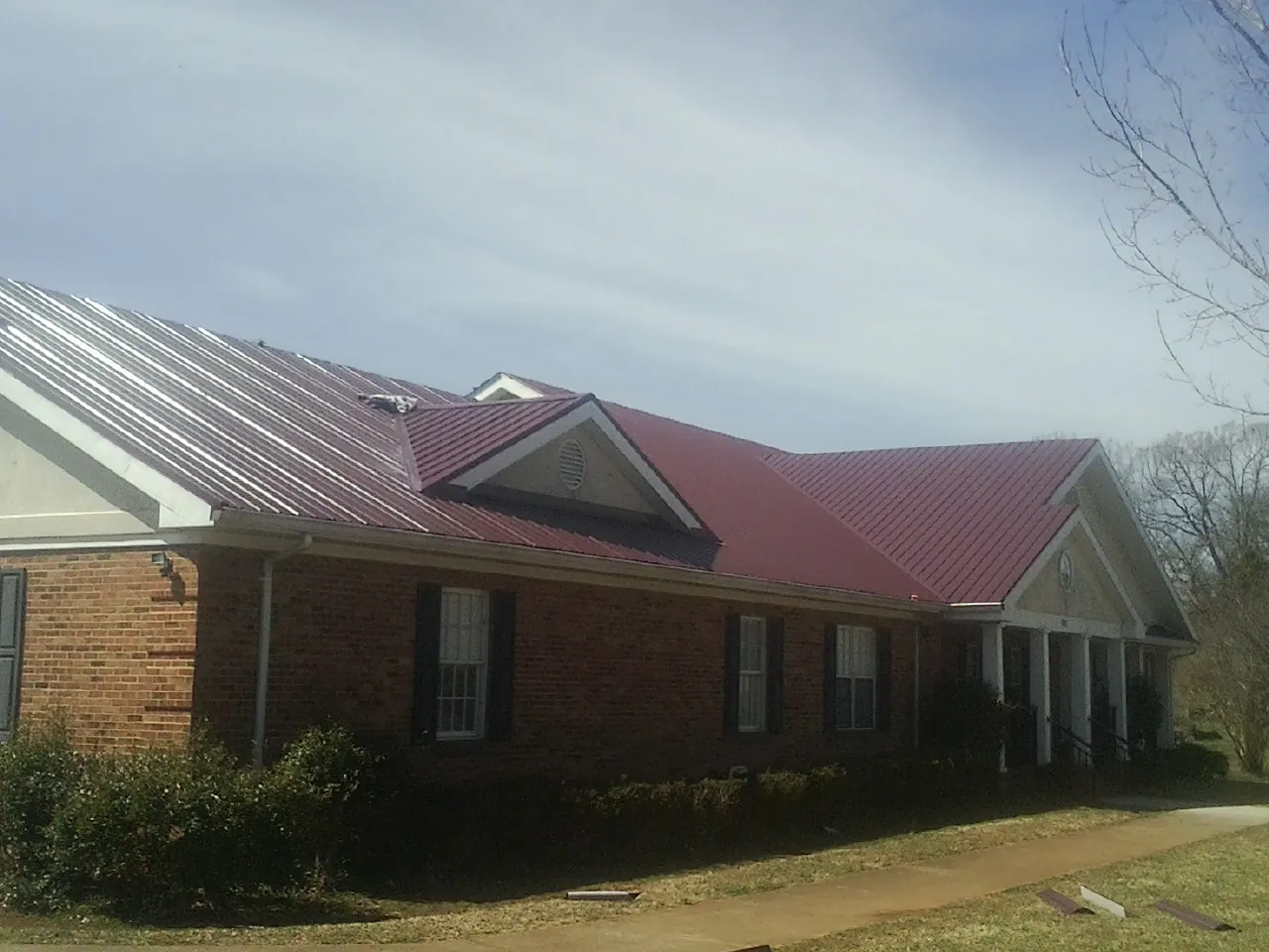 Red metal roof with gabled entries on a long brick building, from a Hail Damage Roof Repair job in Poland