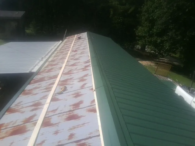 Old rusted panels beside newly installed green metal roofing — Wind Damage Roof Repair by Roofing Brothers in Poland