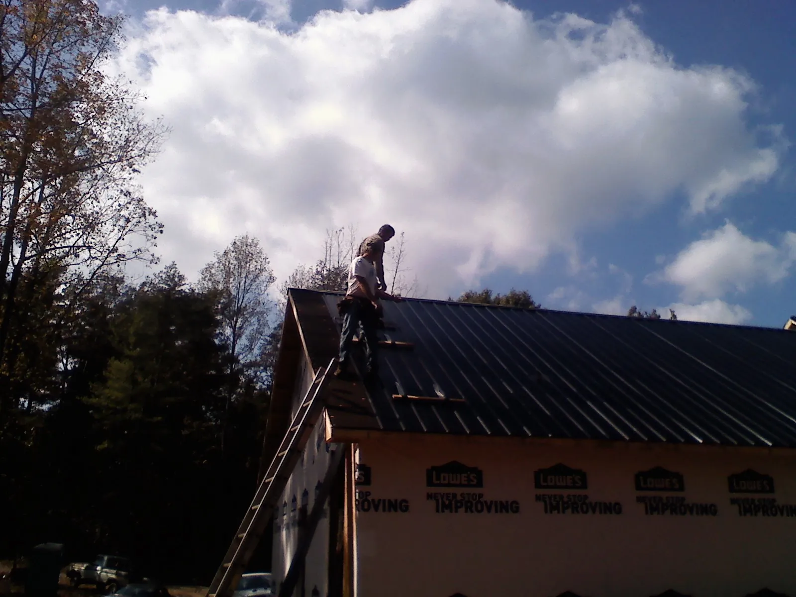 Roofer fastening dark metal panels high against a cloudy sky, from a Roof Inspection job in Poland
