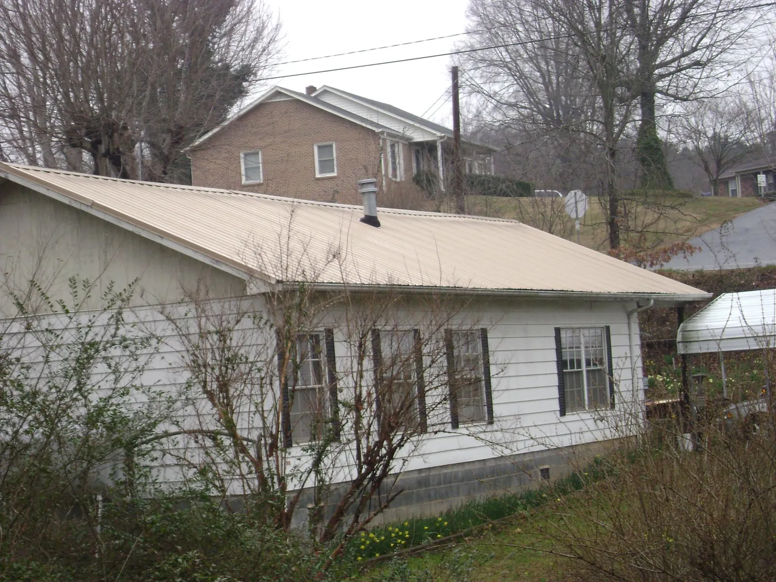 Tan metal roof on a white sided house set into a hillside — Commercial Roofing by Roofing Brothers in Poland